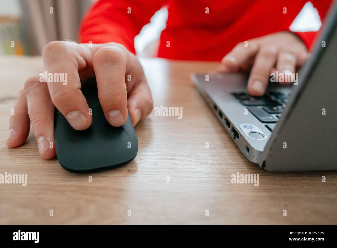 Nahaufnahme einer Hand, die auf eine Computermaus klickt, während die andere Hand auf eine Laptop-Tastatur drückt. Szene im Büro oder zu Hause. Konzept der Fernbedienung Stockfoto