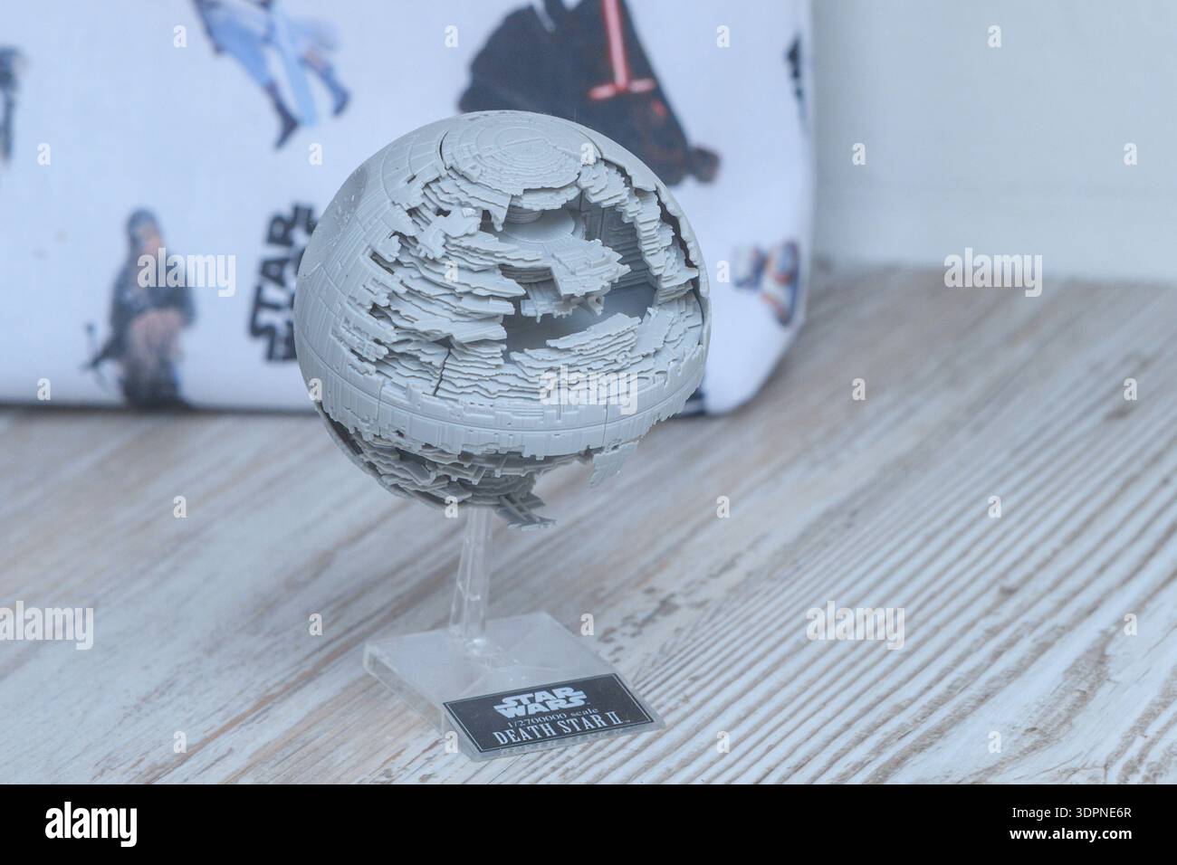 Unbekannter Ort - 12. Mai 2021: Ein detailliertes Modell des Star Wars Death Star II ist auf einer Holzoberfläche zu sehen, mit einem Star Wars-Thema-Stoff mit Charakterillustrationen im Hintergrund. Stockfoto