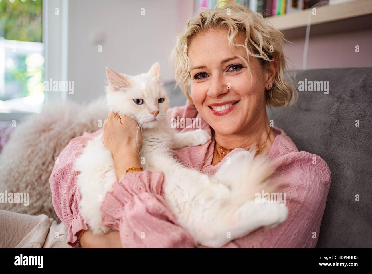 Frau mit flauschiger weißer Katze, die zu Hause lächelt Stockfoto
