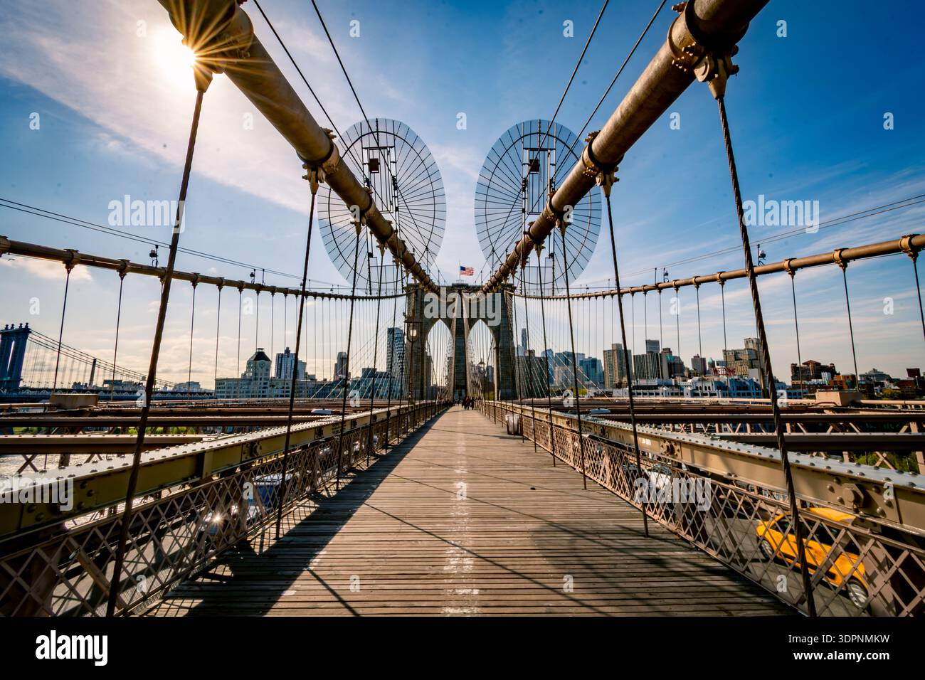 Symmetrische Perspektive auf den hölzernen Fußgängerweg der Brooklyn Bridge mit Hängeseilen, die unter klarem Blau zur Skyline von Manhattan führen Stockfoto