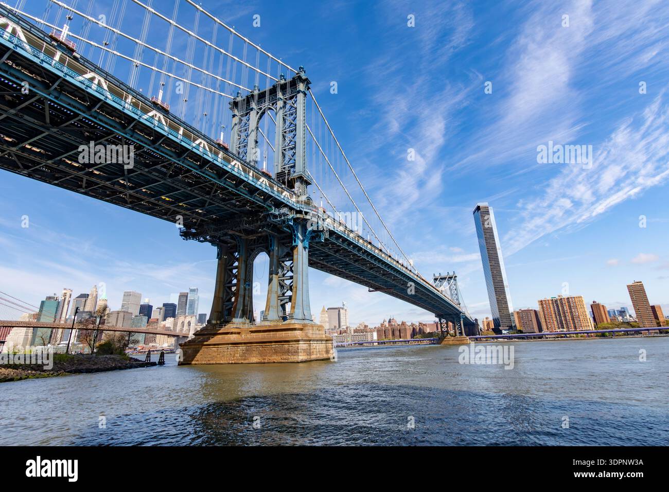 Weitwinkelblick auf die Manhattan Bridge über den East River mit der Skyline von New York City im Hintergrund. Legendäre Hängebrücken-Architektur unter Stockfoto