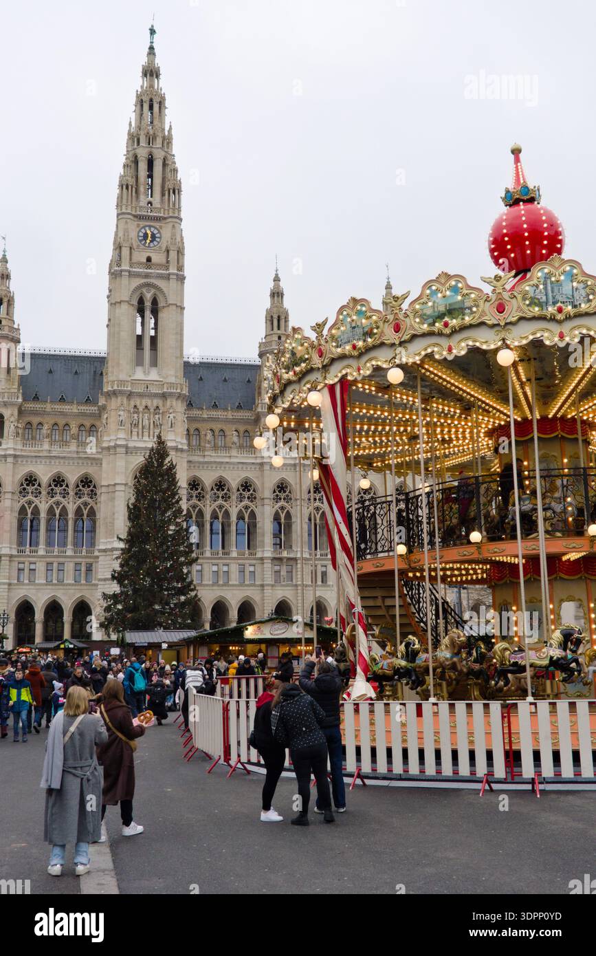 Ein beleuchtetes Karussell auf dem Wiener Weihnachtsmarkt am Rathausplatz mit dem gotischen Wiener Rathaus im Hintergrund. Stockfoto
