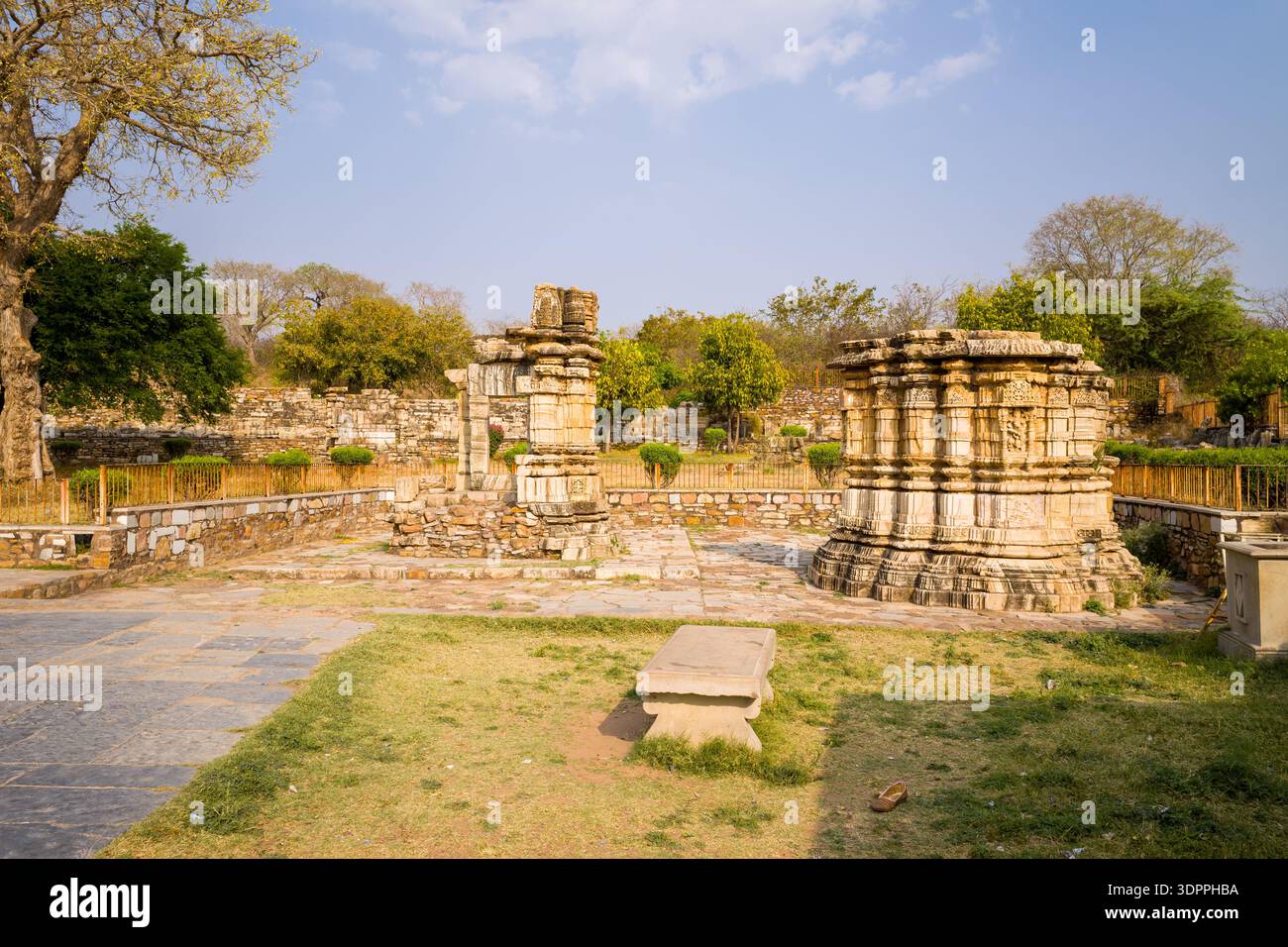 Chittorgarh, Indien - 21. März 2022: Das Bild zeigt die Überreste von antiken Steinstrukturen und Säulen im Tempel Baan Mata, mit geschnitzten Basen und Teilsäulen, umgeben von einer Steinmauer und Grün unter klarem Himmel. Stockfoto