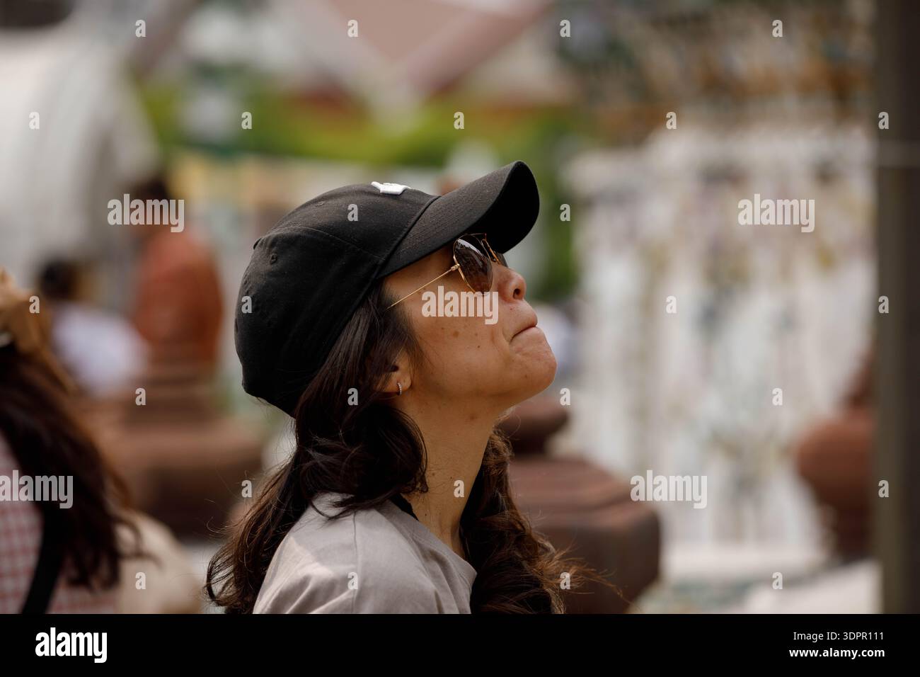 BANGKOK, THAILAND-21. JAN 2026: Weibliche Touristen mit schwarzer Kappe stehend und aufblickend, Hautstruktur im Gesicht, Seitenprofil, im Wat Arun. Stockfoto