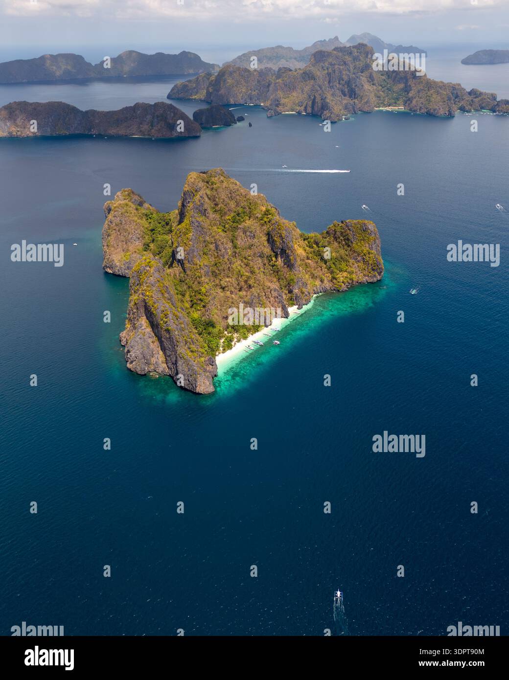Ein Blick aus der Vogelperspektive zeigt eine steile Kalksteininsel mit freiliegenden Felswänden und einen schmalen weißen Sandstrand, umgeben von klarem türkisfarbenem Wasser. Stockfoto