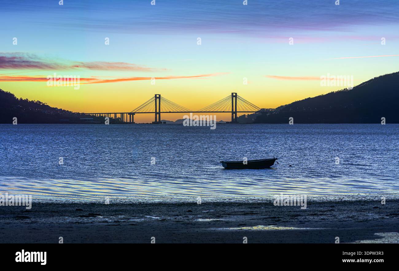 Kleines Ruderboot in der ruhigen Vigo-Mündung bei Sonnenuntergang mit der Silhouette der Rande-Brücke und der Cíes-Inseln im Hintergrund, Cesantes, Galicien, Sp Stockfoto