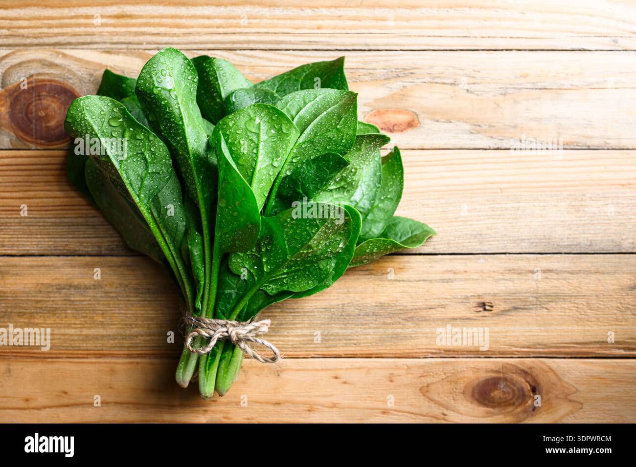 Feuchte Spinatblätter bündeln sich auf Holztisch mit Wassertröpfchen. Frische Produkte, Küchenzubereitung und nachhaltiges Lifestyle-Konzept Stockfoto