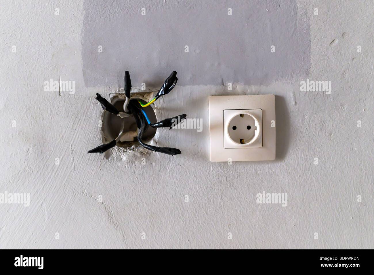Freiliegende elektrische Drähte im Wandloch neben der Steckdose, unsichere Installation, selektiver Fokus Stockfoto