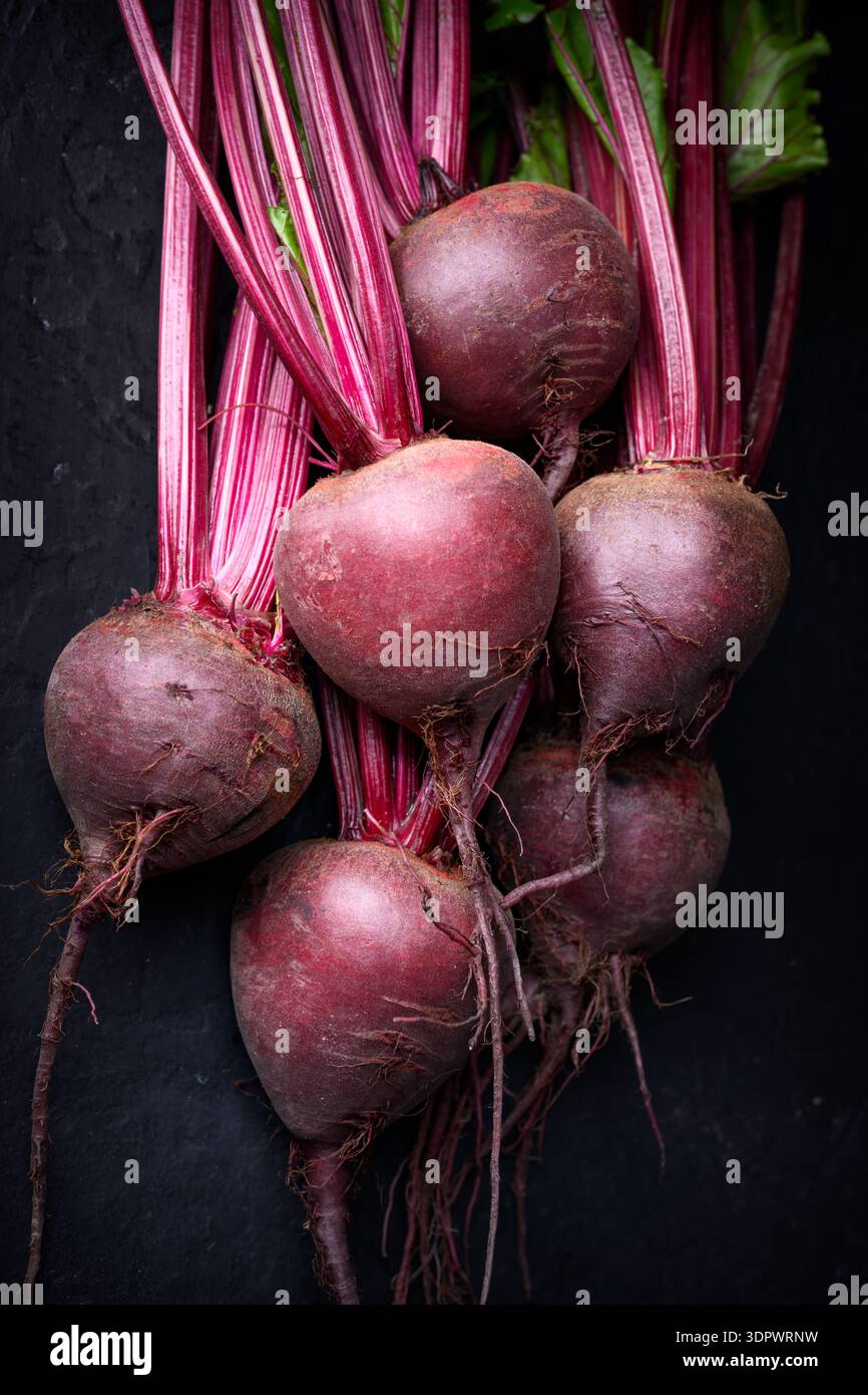 Rohe Rote Bete mit Blättern auf dunkler Oberfläche. Frische Bio-Gemüsekost mit natürlicher Textur Stockfoto