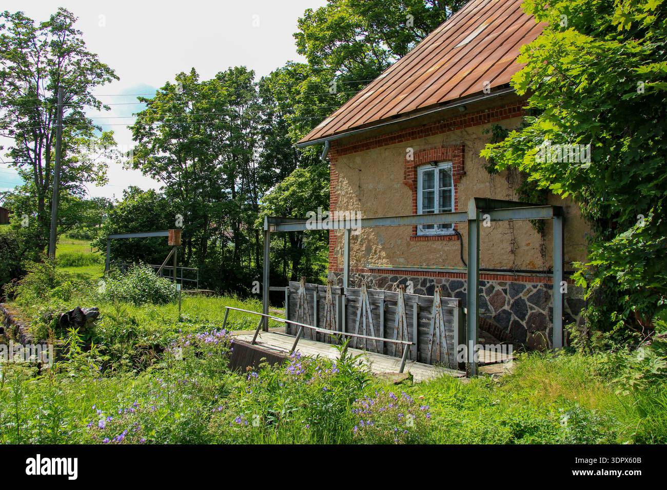 Rustikales Mühlenhaus in einer üppigen Landschaft mit einer traditionellen Wasserschleuse daneben. Das Gebäude hat eine bräunlich-rote Ziegelfassade mit einem Sto Stockfoto