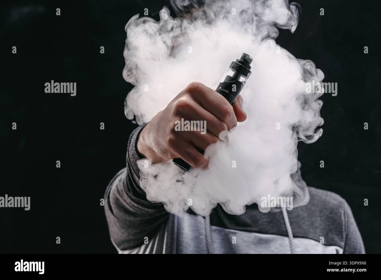 Die Hand hält das Vape Device, während eine große Wolke aus Dampf in einer dunklen Umgebung freigesetzt wird Stockfoto