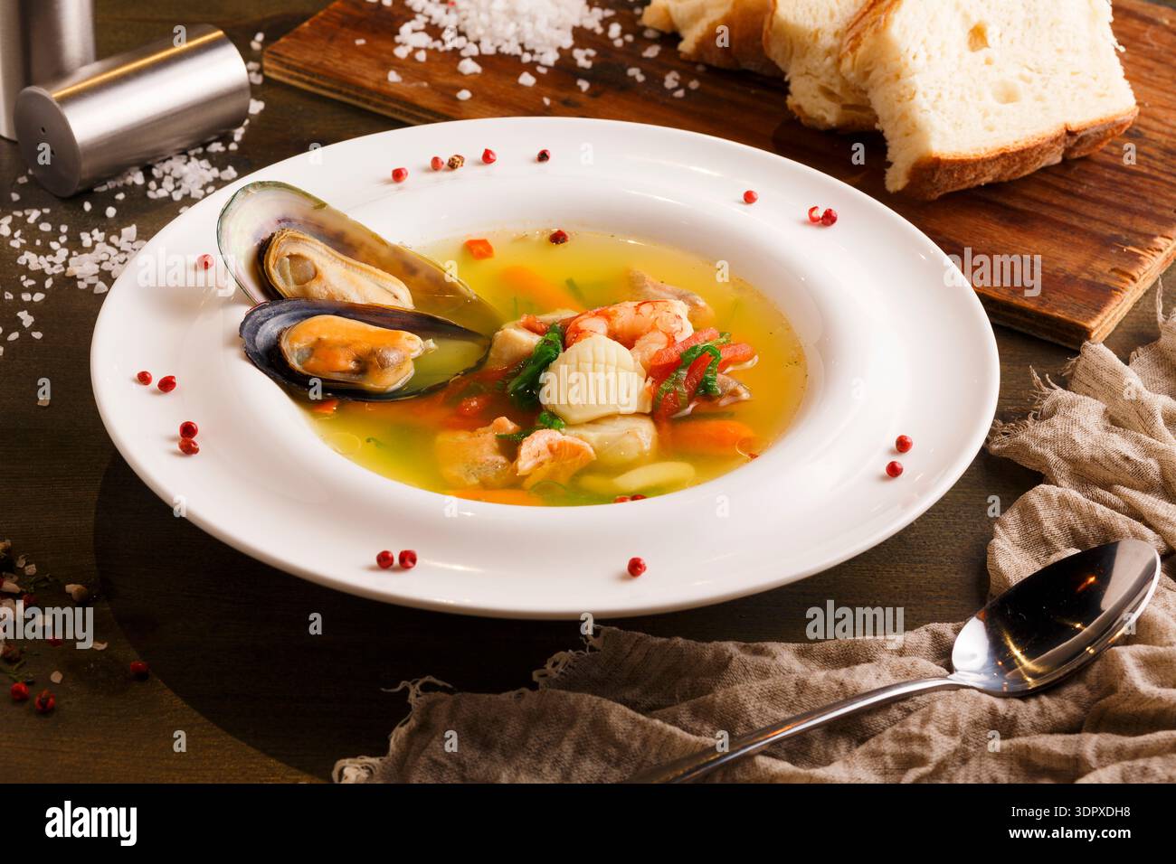 Meeresfrüchte-Suppe auf einem weißen Teller, serviert mit Brot auf einem Holztisch Stockfoto