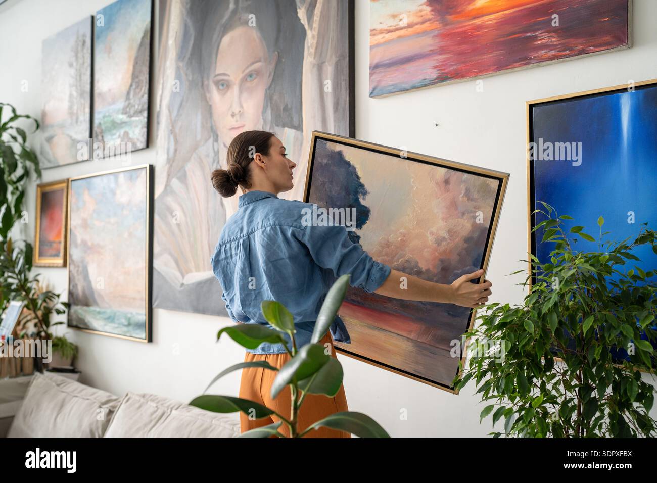 Fokussierte, geschickte Künstlerin, die Gemälde an die Wand hängte, gefüllt mit Ausstellung eigener Meisterwerke. Stockfoto
