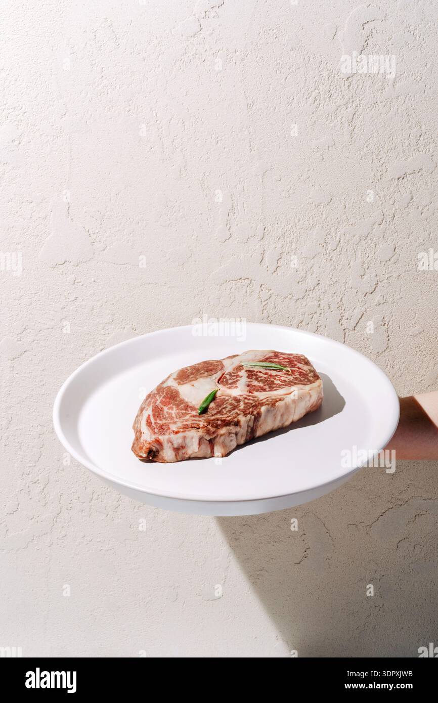 Ein hochwertiges Ribeye-Steak aus Wagyu-Rindfleisch, nass gereift für einen besseren Geschmack, auf einer weißen Platte. Die Marmorierung und der Reichtum des Steaks sind ein Highlight Stockfoto