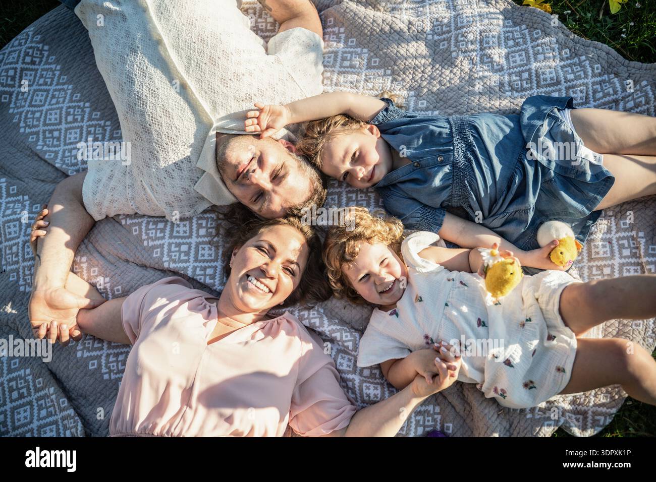 Eine glückliche Familie von vier Personen, darunter ein Mann, eine Frau und zwei Mädchen, feiert fröhlich Ostern. Sie liegen draußen auf einer Picknickdecke und genießen die Stockfoto