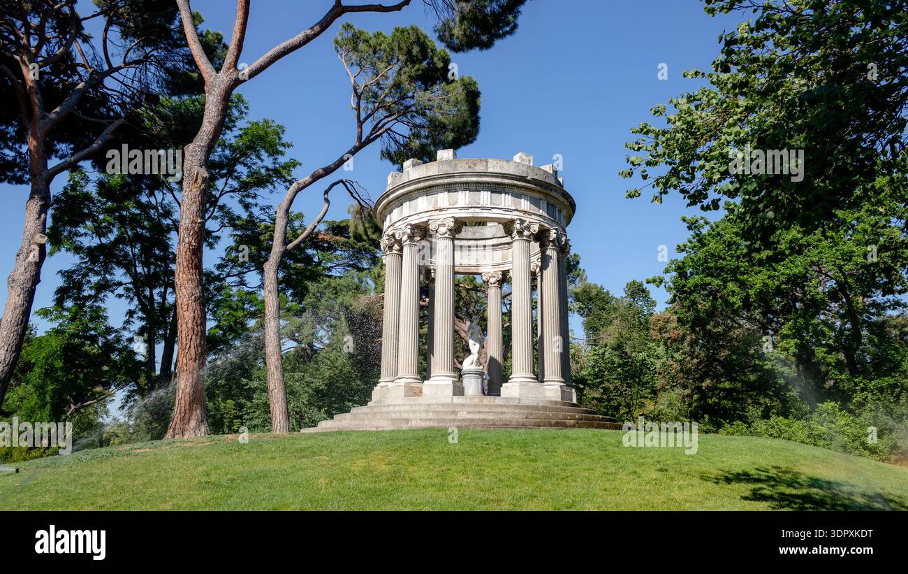Der malerische Tempel, umgeben von üppigem Grün, im El Capricho Park in Madrid, Spanien, bietet eine ruhige Zuflucht. Hohe Bäume und gepflegte Rasenflächen runden das Angebot ab Stockfoto