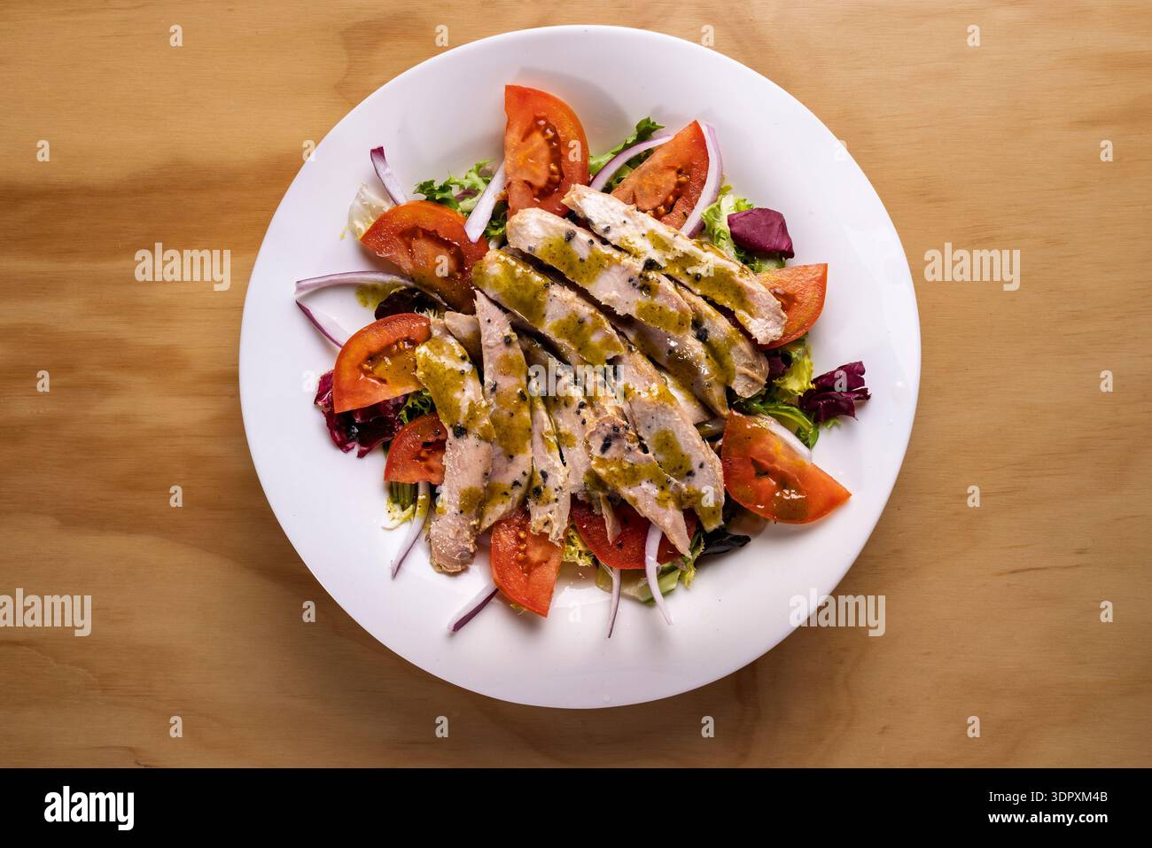 Ein köstlicher Teller Thunfischbauch-Salat mit frischen Kirschtomaten, knusprigen roten Zwiebeln und aromatischem Basilikum, alles in süßem Honig und Pistazien gekleidet Stockfoto