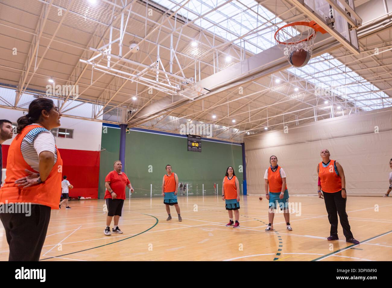 Männer und Frauen mit intellektuellen Behinderungen beobachten während des inklusiven Trainings einen Basketballschuss. Adaptiver Sport fördert Teamarbeit, Selbstvertrauen und Wohlbefinden Stockfoto