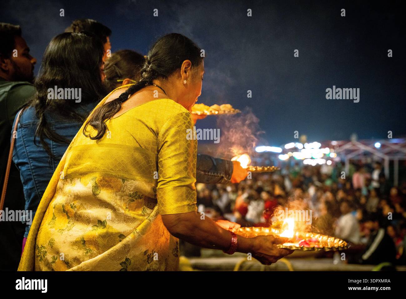 Indische Frau in gelbem Saree spielt aarti mit Öllampen während einer lebhaften Nachtfestzeremonie. Stockfoto