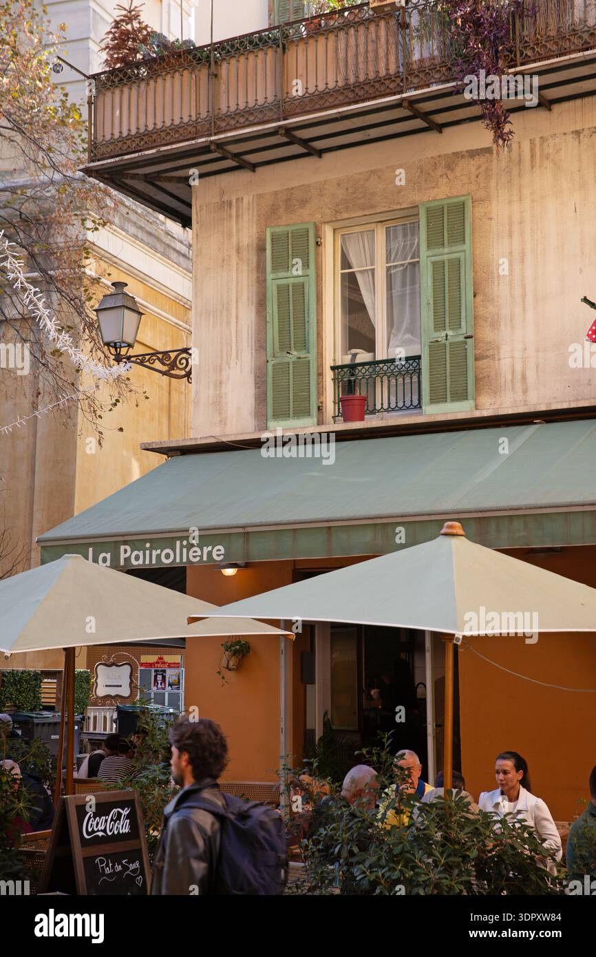 Café La Pairolière in Nizza, Frankreich, mit grünen Fensterläden, schmiedeeisernem Balkon und Außenterrasse im warmen Nachmittagslicht. Stockfoto