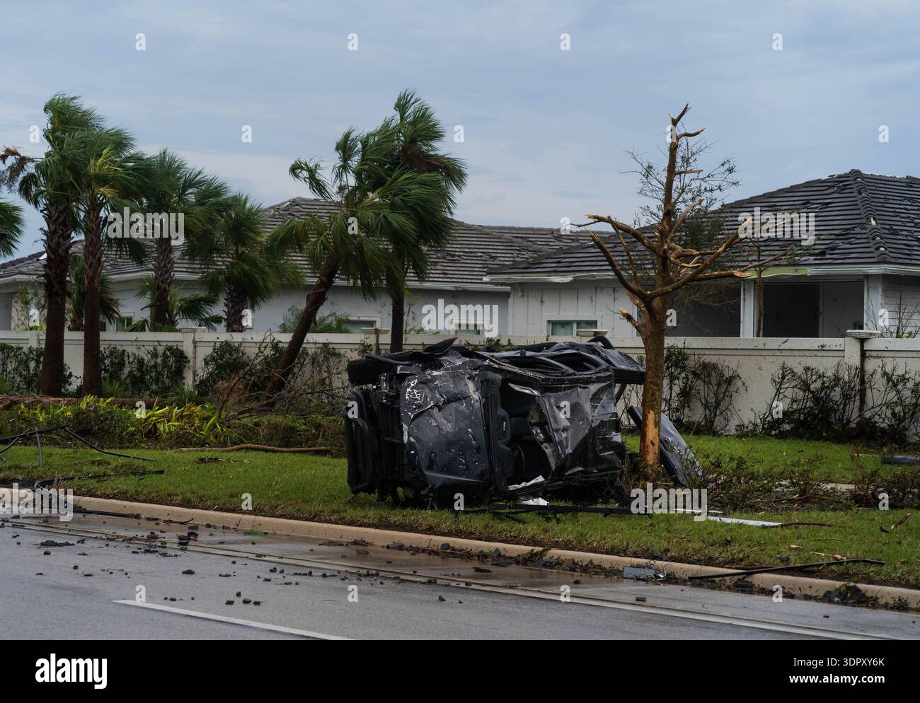 Palm Beach Gardens, USA - 09. Oktober 2024: Blick auf ein umgekipptes Fahrzeug inmitten von Schutt übersäter Rasenflächen mit beschädigten Palmen und Häusern Stockfoto
