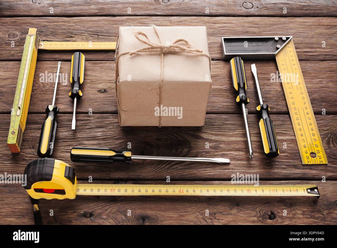 Werkzeuge, die um ein verpacktes Paket auf Holzoberfläche angeordnet sind, für die Vorbereitung von Heimwerkerprojekten Stockfoto