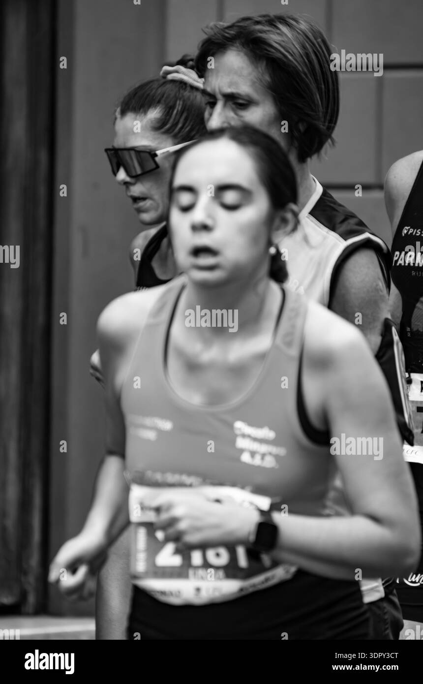 Dramatisches Schwarzweißbild, das die Müdigkeit und Entschlossenheit von Läuferinnen feststellt, die an einem italienischen Halbmarathon mit engen Rahmen und en teilnehmen Stockfoto