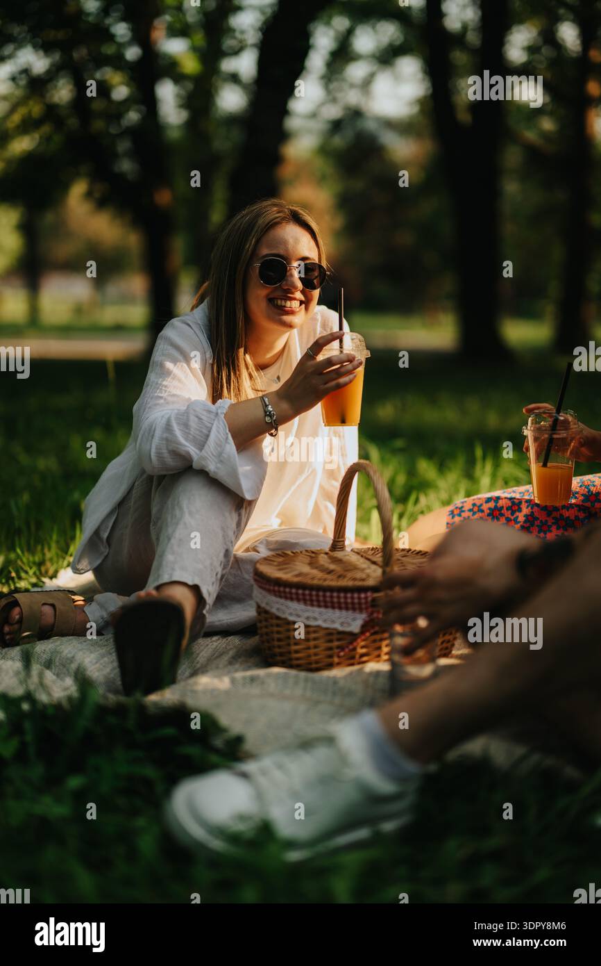 Frau genießt ein sonniges Picknick in einem Park mit Orangensaft und Freunden Stockfoto