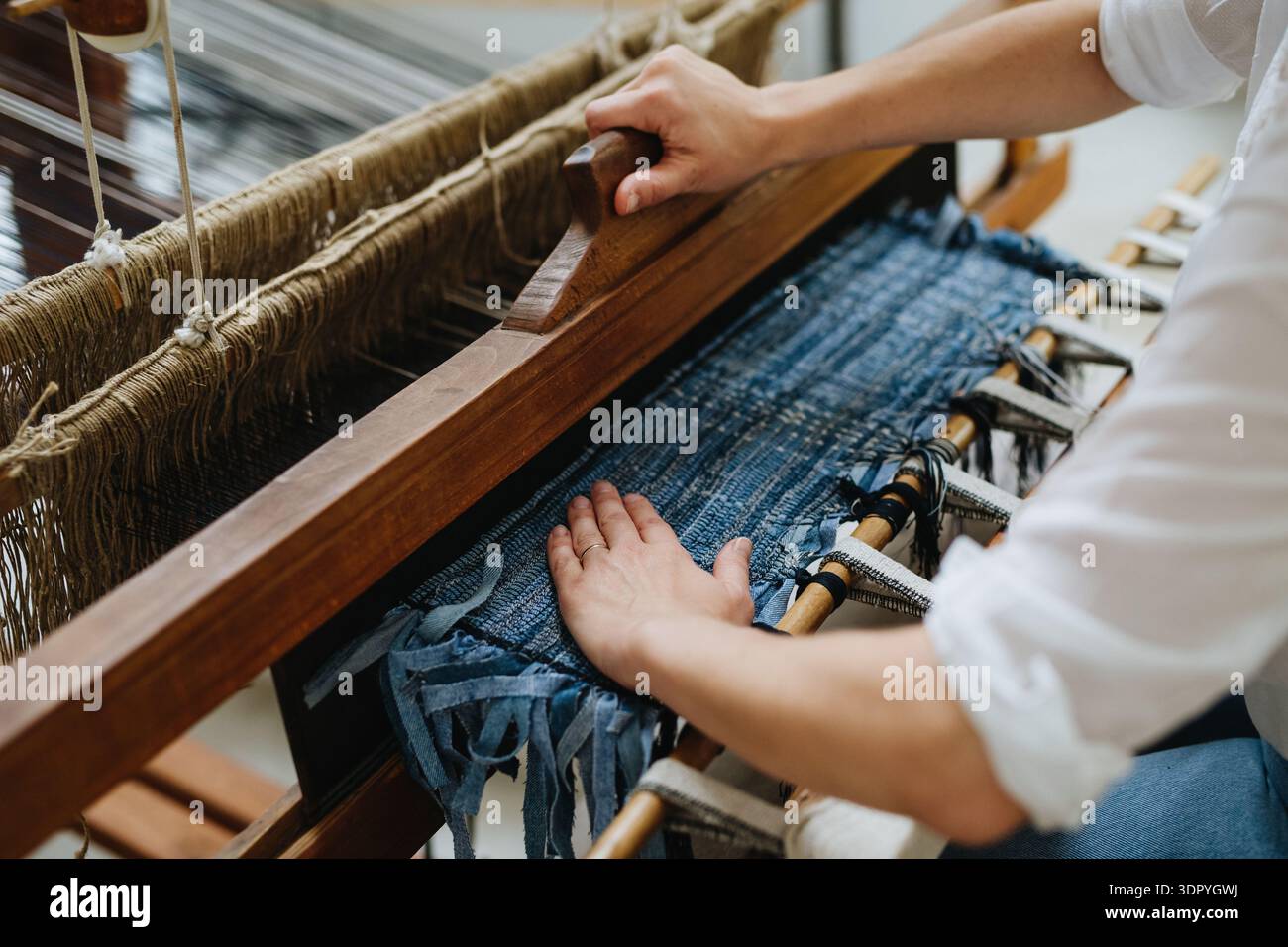 Nahaufnahme einer Frau, die an Holzwebstühlen arbeitet und einen Teppich aus alten Stoffen webt. Aufschwung in Unternehmen und Kreislaufwirtschaft. Stockfoto