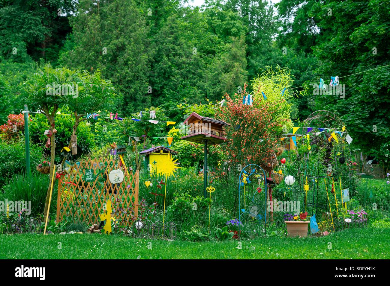 Heller kreativer Garten mit Vogelhäusern, Blumen und handgefertigten Dekorationen. Üppiges Grün und leuchtende Farben in gemütlicher Umgebung im Hinterhof. Stockfoto