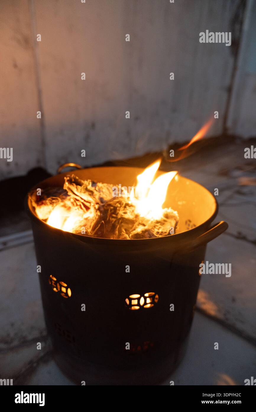 Brennendes Feuer im Metalleimer mit glühender Glut, rustikale Außenumgebung, warmes Umgebungslicht, Nachtszene Stockfoto