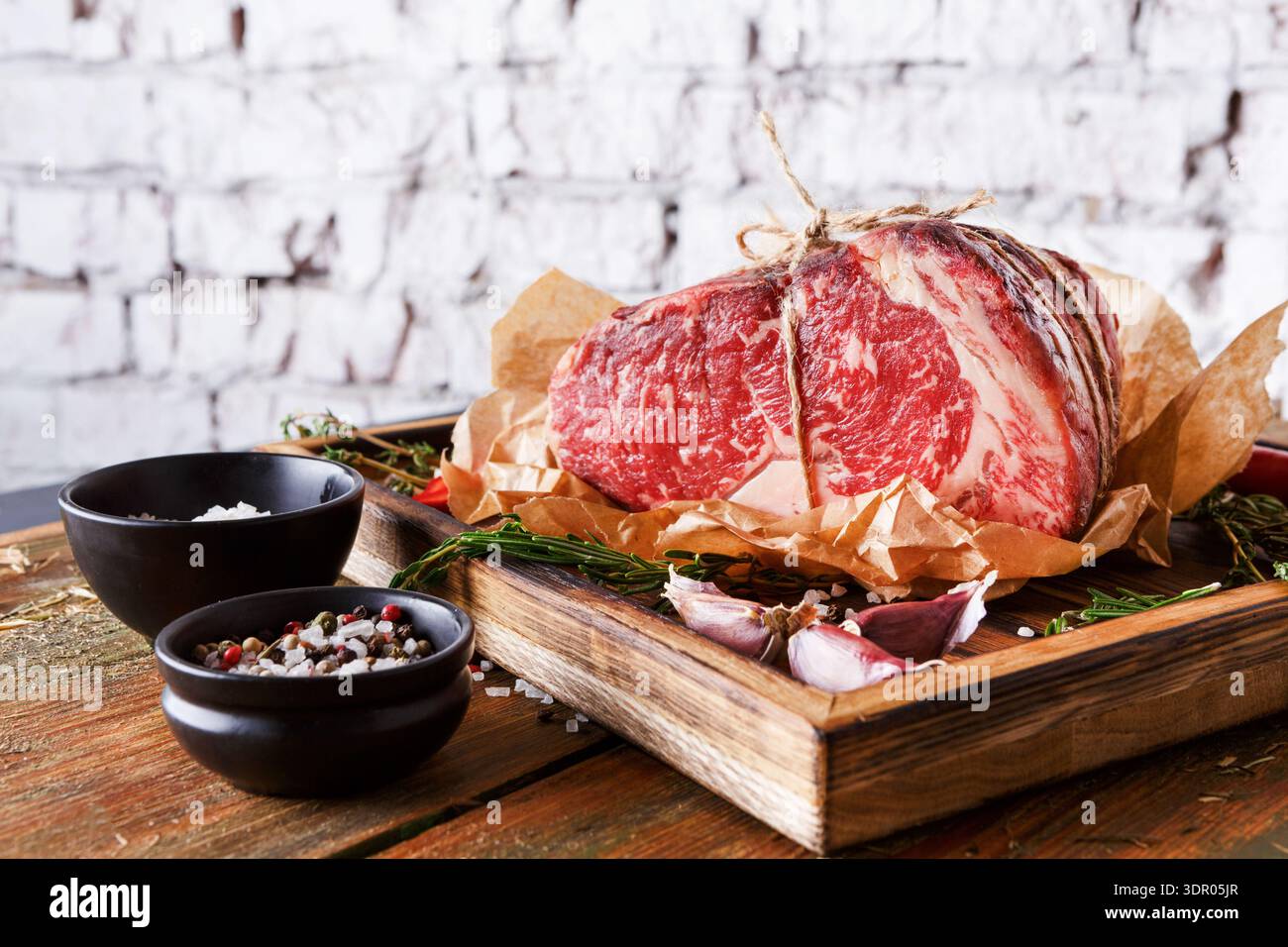 Hochwertiges Rindfleisch auf Holzbrett mit Gewürzen und Dekorationen auf dem Tisch Stockfoto