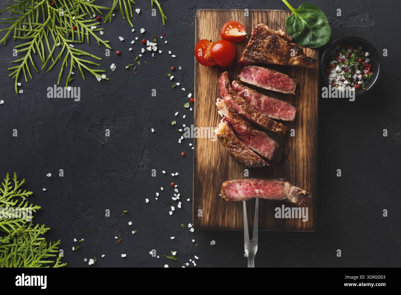 Gegrilltes Steak auf einem Holzbrett mit Tomaten und Kräutern an einem Esstisch Stockfoto