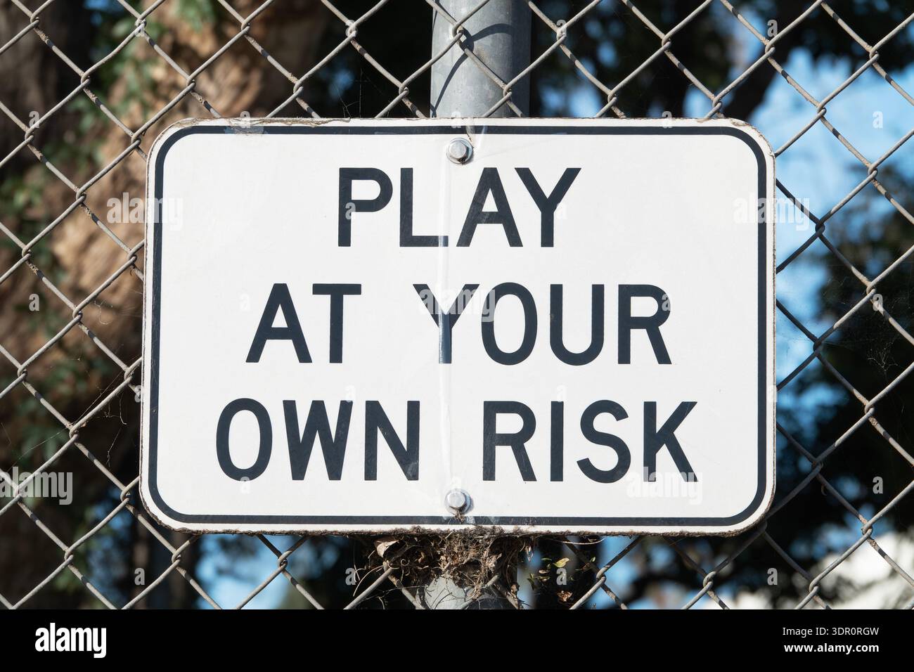 Altes Spiel auf eigene Gefahr Schild am Maschendrahtzaun in einem öffentlichen Park. Stockfoto