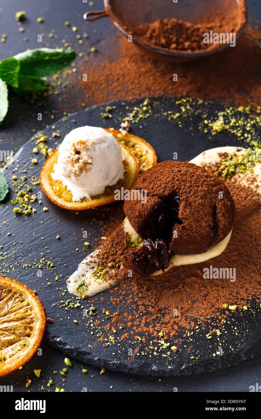 Dessert mit Schokoladenkuchen, Eis und Orangenscheiben auf einem schwarzen Teller Stockfoto
