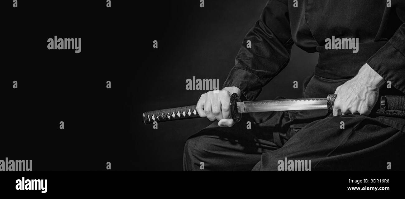 Die Samurai halten ein japanisches Katana-Schwert, ein Banner, in Schwarz und Weiß. Foto eines Kriegers in schwarzer Kleidung mit Platz für Text Stockfoto