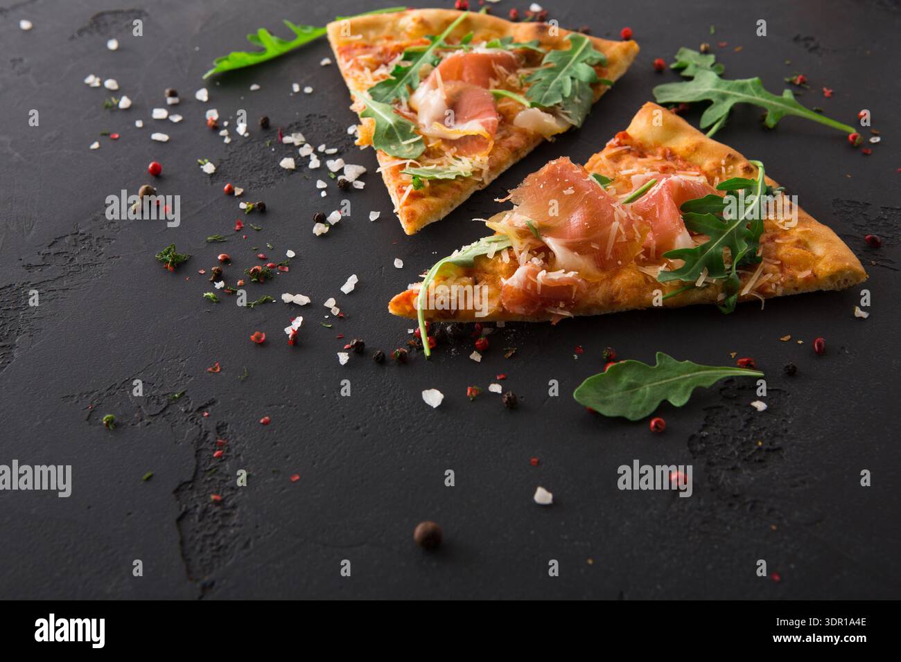 Köstliche Pizzastücke mit Prosciutto und Arugula auf dunklem Hintergrund Stockfoto