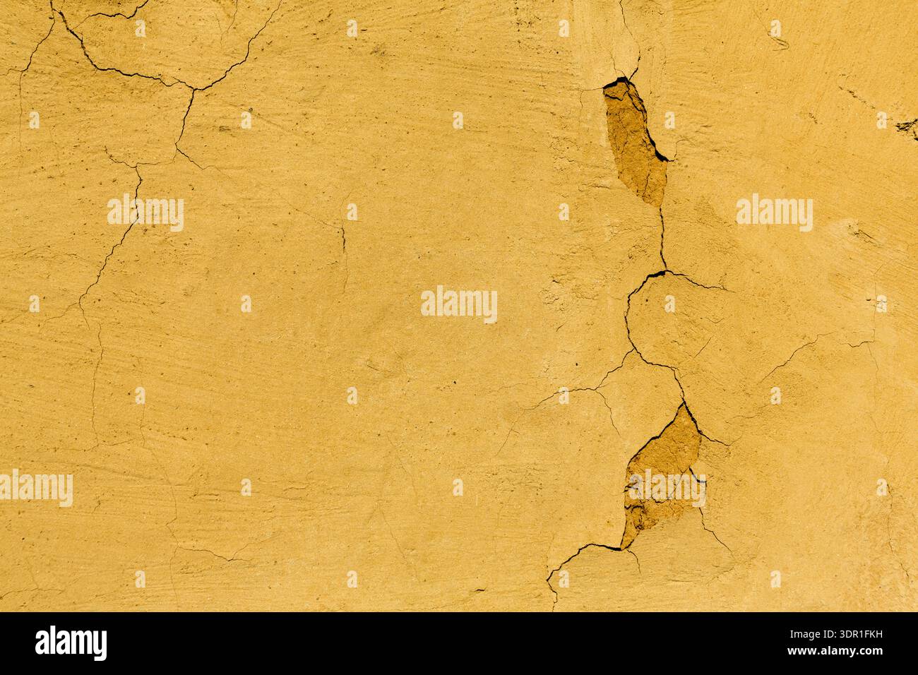Die gerissene gelbe Wand zeigt Abnutzung in ländlichen Umgebungen während der Tageslichtstunden Stockfoto
