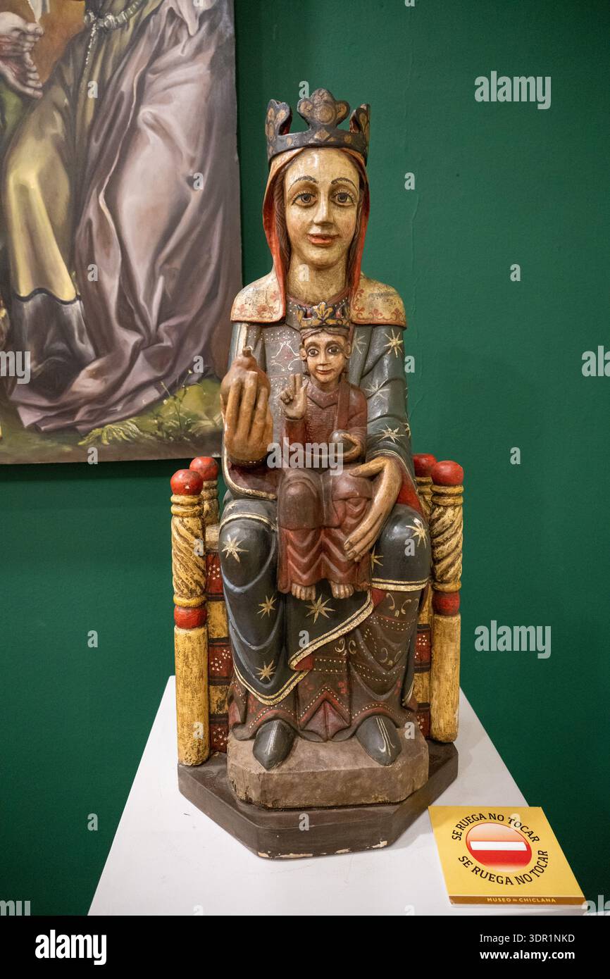 Chiclana, Spanien 26. September 23: Hölzerne gekrönte madonna und Kinderstatue auf Ausstellungssockel im Museum, religiöse Volkskunst, grüner Wandhintergrund, sanfte li Stockfoto