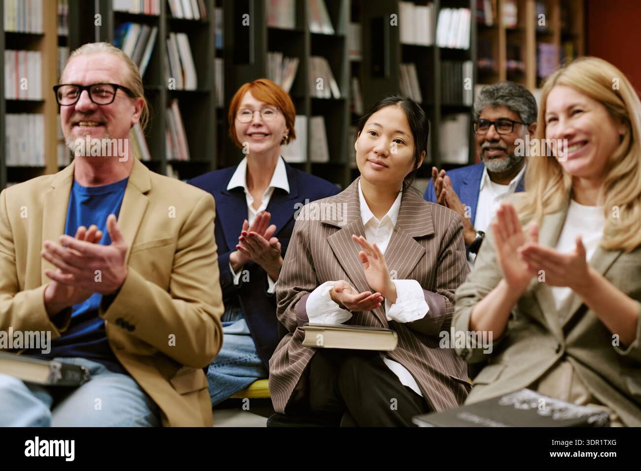 Multiethnische Gruppe von Erwachsenen, die nach der Buchpräsentation applaudieren Stockfoto