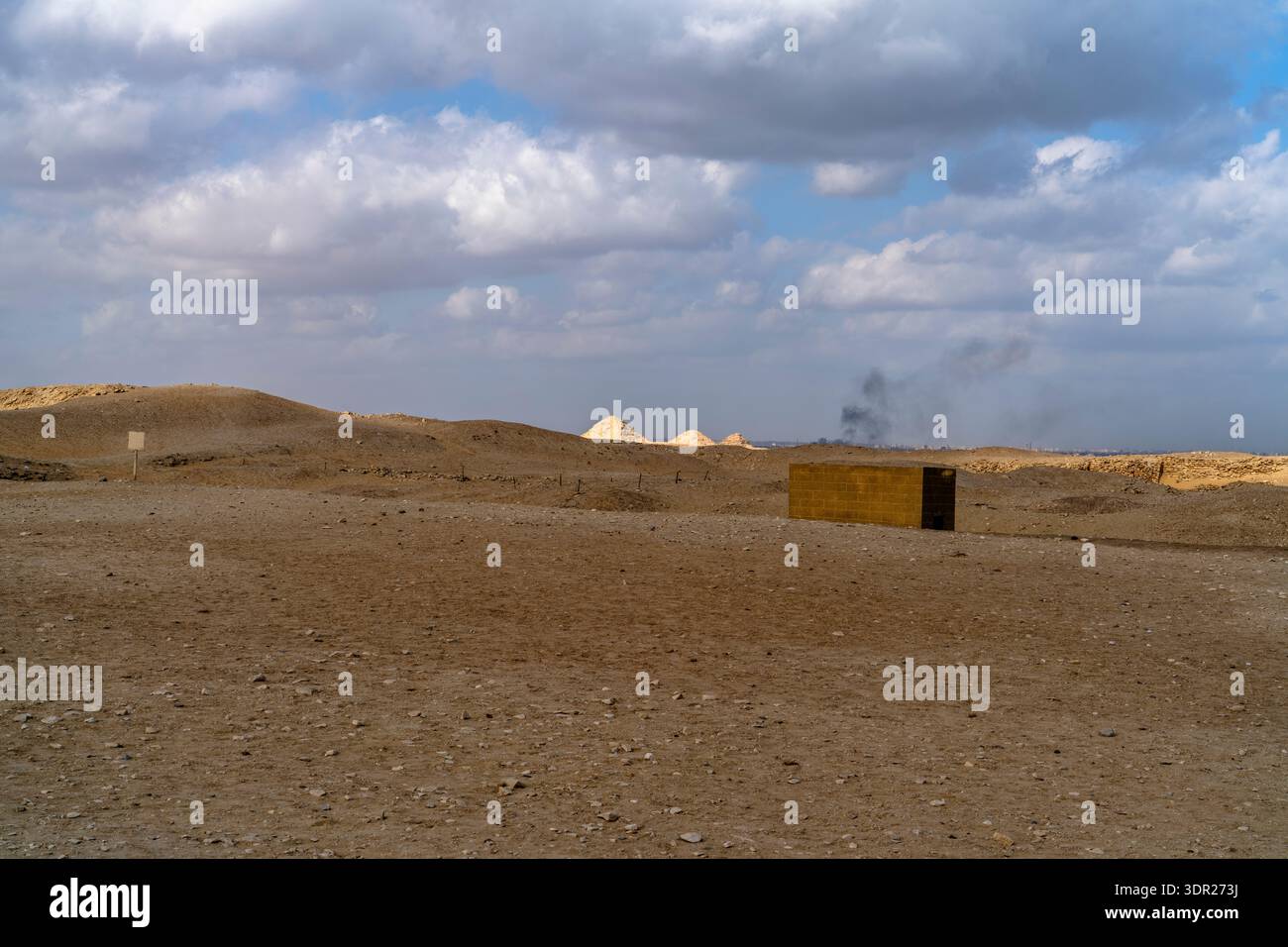 Weite Wüstenebene in der Nähe von Kairo, Ägypten, mit einer kleinen Steinstruktur und fernen Hügeln unter einem bewölkten Himmel, die Isolation, Größe, trockenes Klima betonen Stockfoto