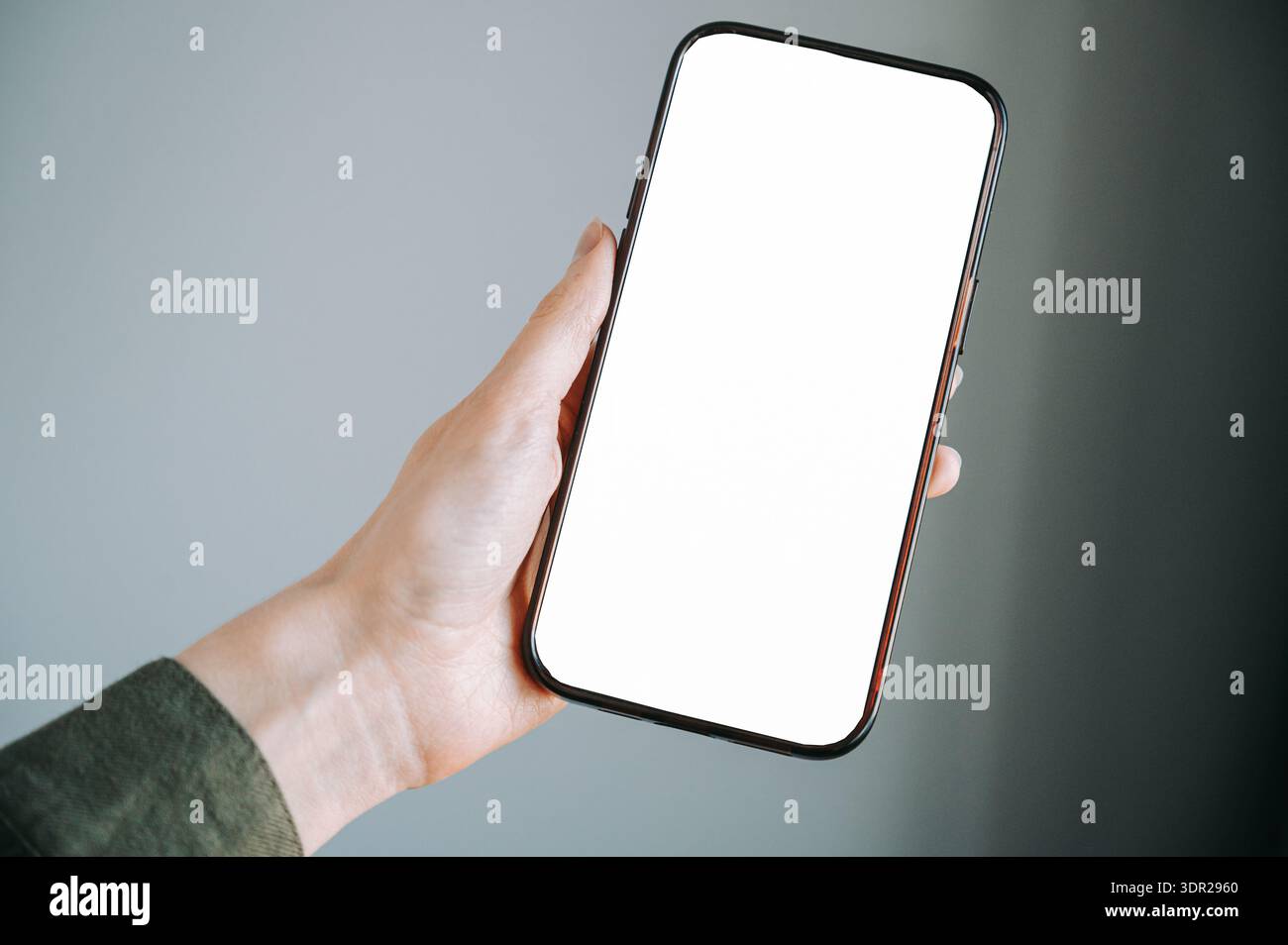Nahaufnahme einer Hand, die ein modernes Smartphone mit einem leeren weißen Bildschirm hält. Dank minimalem Hintergrund und Kopierraum ist dieses Bild ideal für das Presen von Apps Stockfoto