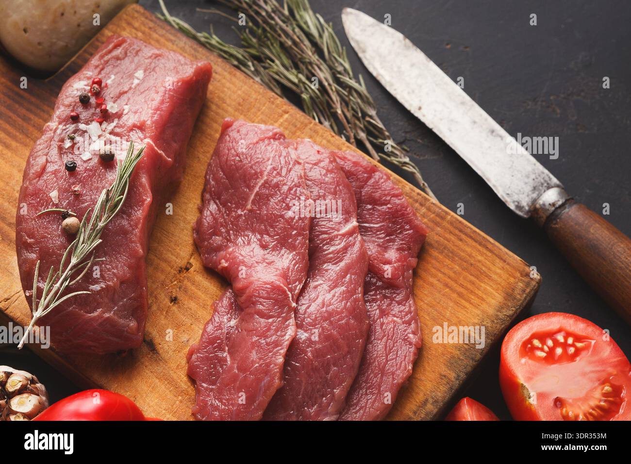 Auswahl an rohem Rindfleisch und frischen Zutaten auf einem Holzbrett in einer Küche Stockfoto