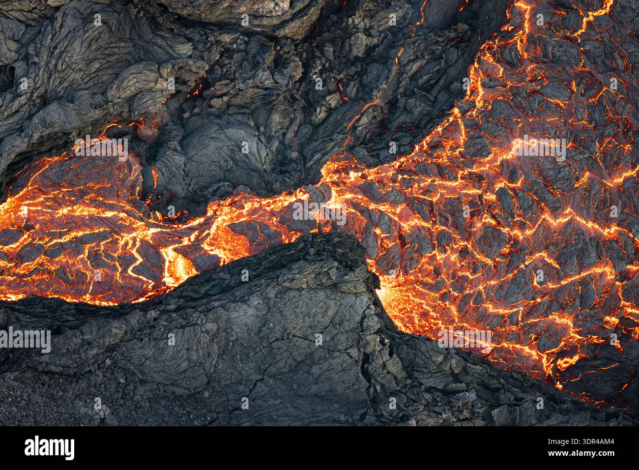 Aus der Vogelperspektive der geschmolzenen Lava schlängelt sich durch das dunkle, strukturierte vulkanische Gestein der Reykjanes-Halbinsel, ein feuriger Tanz der Zerstörung und Schöpfung, GRI Stockfoto
