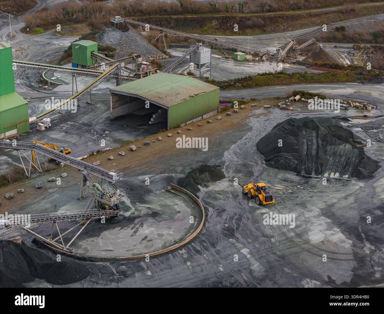 Aus der Vogelperspektive eines großen industriellen Steinbruchs offenbart sich eine Landschaft aus starken Kontrasten, in der schwere Maschinen die Erde inmitten von Haufen von Rohmaterial modellieren Stockfoto