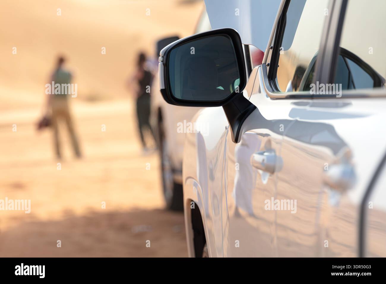 Regionale Abenteueridentität als Nahaufnahme des Seitenspiegels des SUV, der das Wüstenlicht in der Nähe von Dubai, VAE, reflektiert. Verschwommene Touristen im Hintergrund, Kontrast zu Mobili Stockfoto