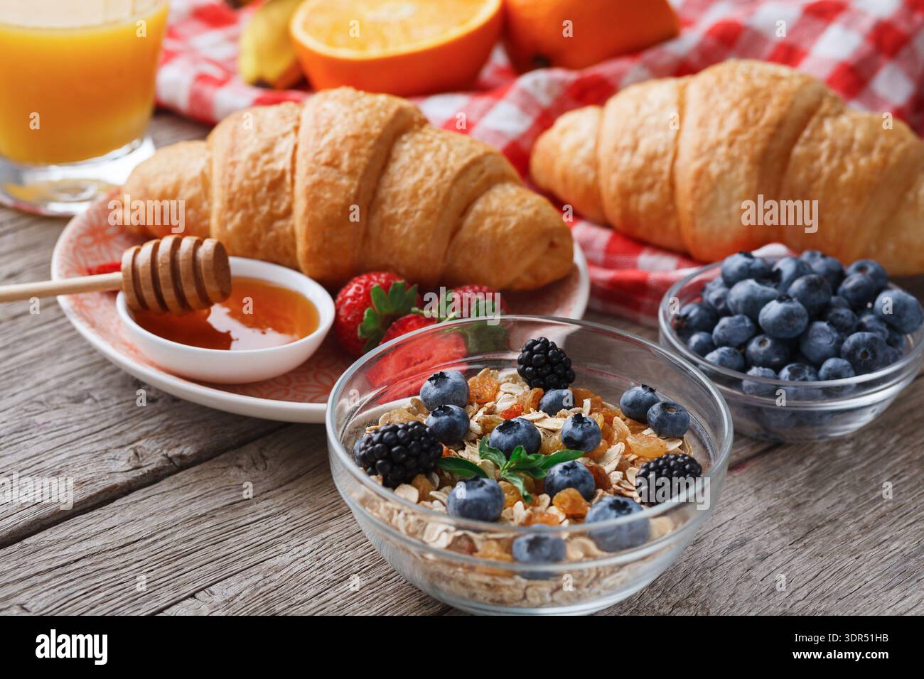 Frühstück mit Croissants, Joghurt, Obst und Honig auf einem Holztisch Stockfoto