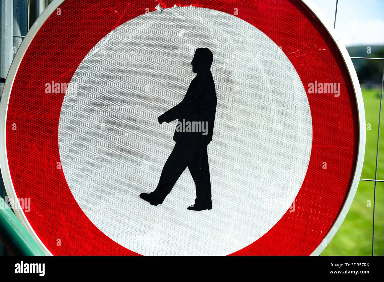 Eine Nahaufnahme eines runden rot-weißen Verbotsschildes mit einer schwarzen Silhouette eines Wandermannes, montiert auf einem Metallzaun im Freien. Stockfoto