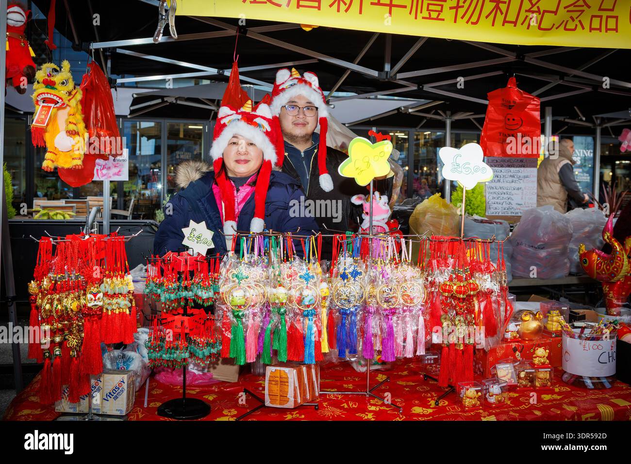 Das Mondneujahrsfest 2026 auf dem Time Square in Warrington feiert das Jahr des Pferdes. Warrington Hongkonger veranstalten eine Show mit Drachentanz, traditionellen Ständen mit Kunsthandwerk, chinesischem Spielzeug und Geschenken sowie Street Food. Klassische Hong Kong Karnevalspiele waren ebenso erhältlich wie kulturelle Erlebnisse wie Fai Chun, chinesische Kalligrafie und Wahrsager. Ein paar Chinesen in Drachenhüten posieren für ein Bild auf ihrem Stand, das chinesische Geschenke verkauft. Quelle: John Hopkins/Alamy Live News Stockfoto