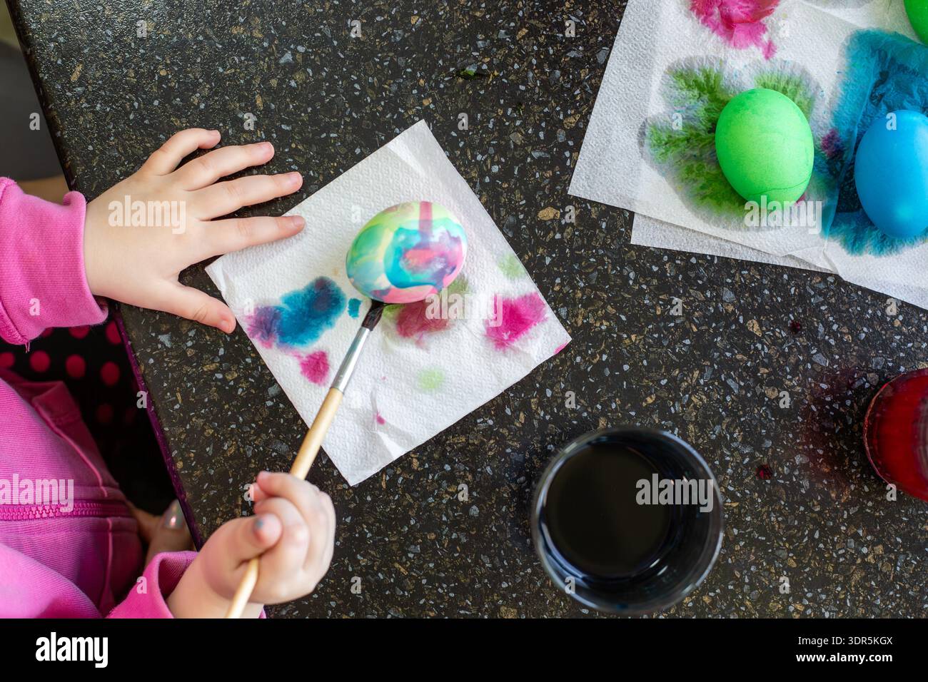 Nahaufnahme der Hände eines Kindes mit einem Pinsel, um ein dekoratives Ei auf eine Serviette zu malen. osterbasteln, Familientraditionen, kreative Kunst. Ostern. Stockfoto